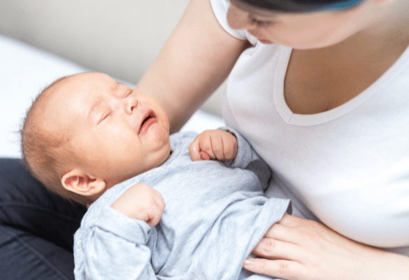un bébé souffre de coliques et pleure dans les bras de sa mère qui lui masse le ventre avec sa main
