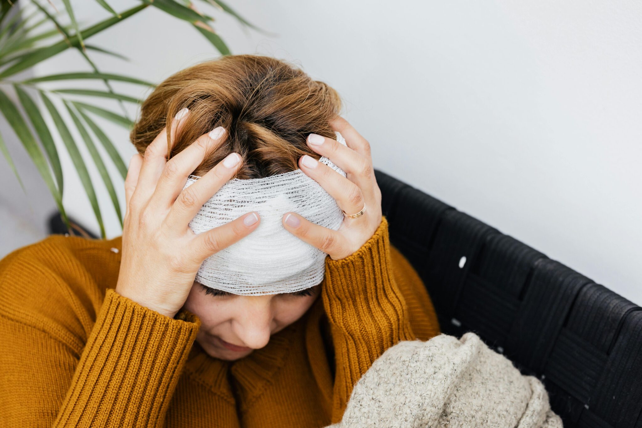 Femme blessée à la tête qui est bandée, et qui la tient entre ses mains
