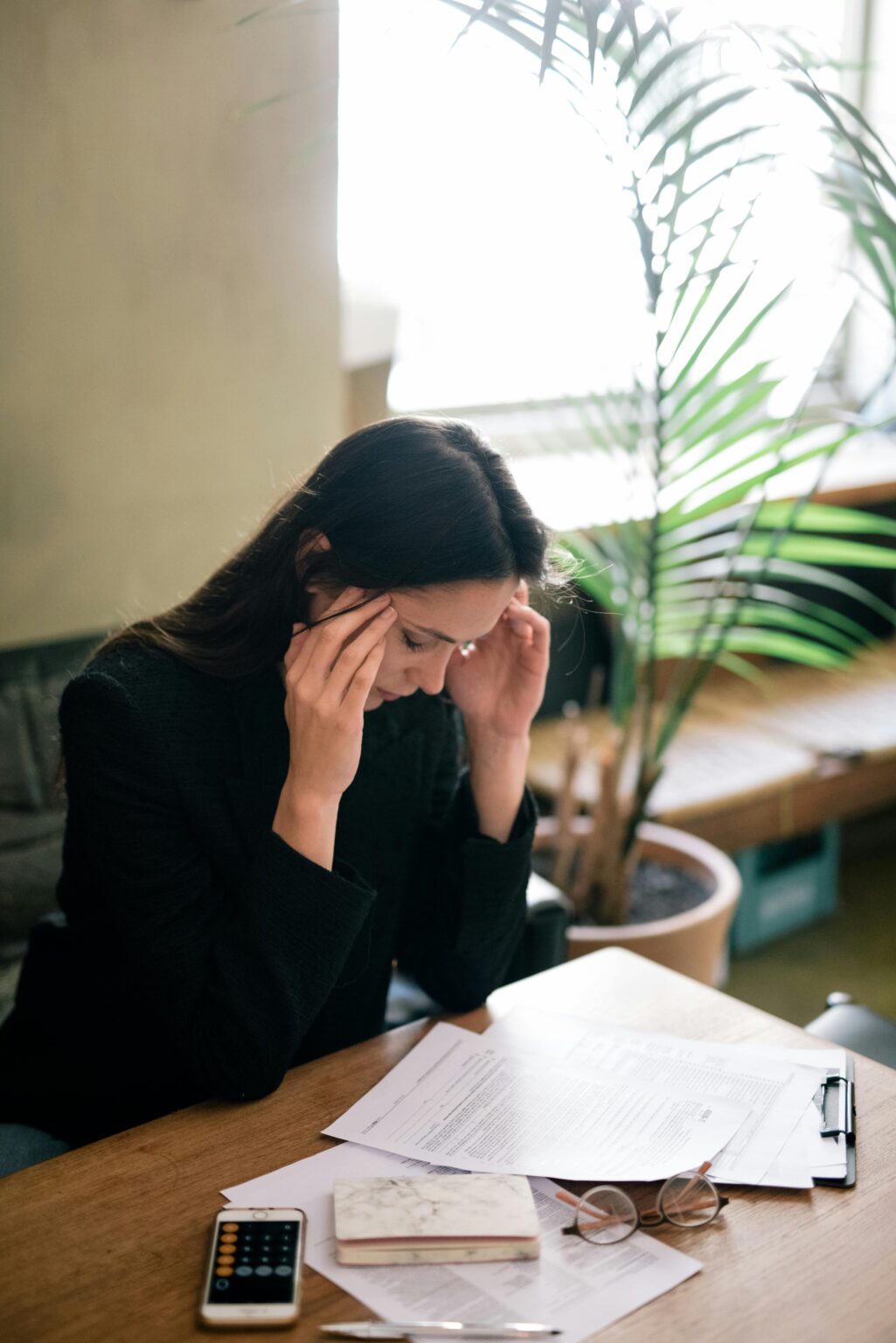 Femme d'affaires assise à son bureau, se tenant les tempes, les yeux fermés, visiblement stressée par son travail et en début de burn-out