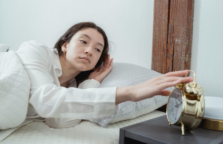 illustration d'une jeune femme en pyjama blanc, allongée dans son lit et éteignant son réveil, le visage fatigué