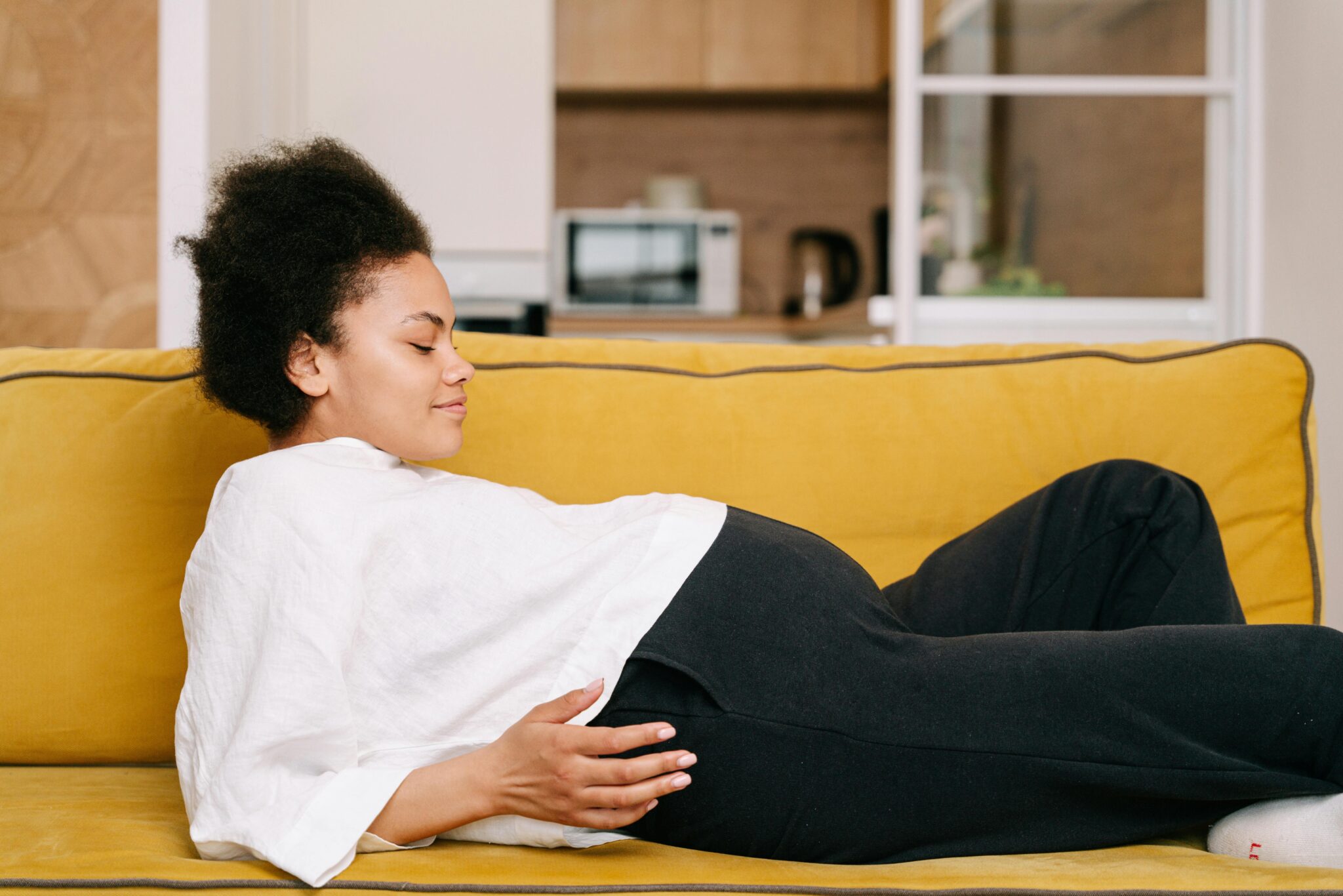 femme enceinte allongée sur le canapé et observant son ventre rond, un sourire aux lèvres