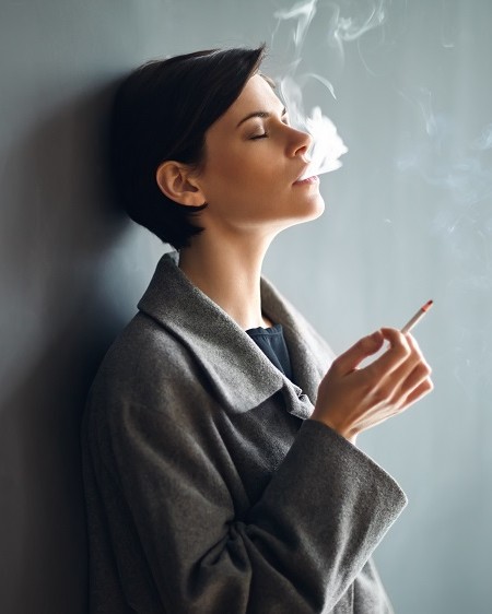 femme qui fume en cachette adossée contre un mur